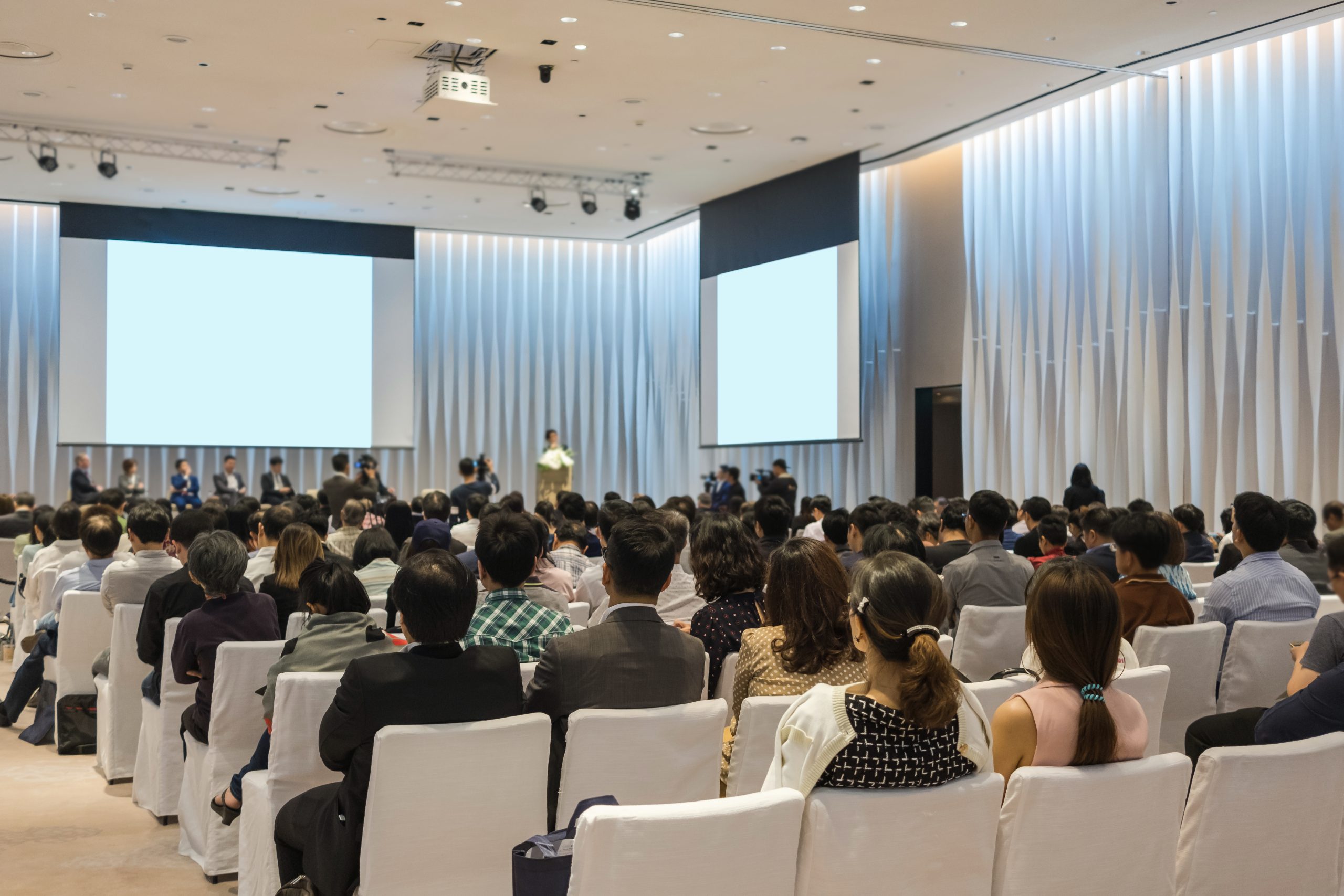 Speakers on the stage with Rear view of Audience in the conferen